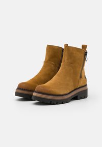 Brown suede ankle boots with a side zipper, flat black treaded sole, and a contrasting brown midsole for added detail and texture.