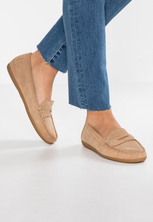 Beige ruskind loafers båret med blå bukser, der er korte ved anklen, på en hvid gulv, der viser side- og frontvisninger af skoene.