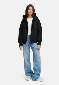 Svart huva-jacka med dragkedja fram och dragsko, kombinerad med ljusblå vida jeans och grå sneakers. Slät tyg och avslappnad passform.