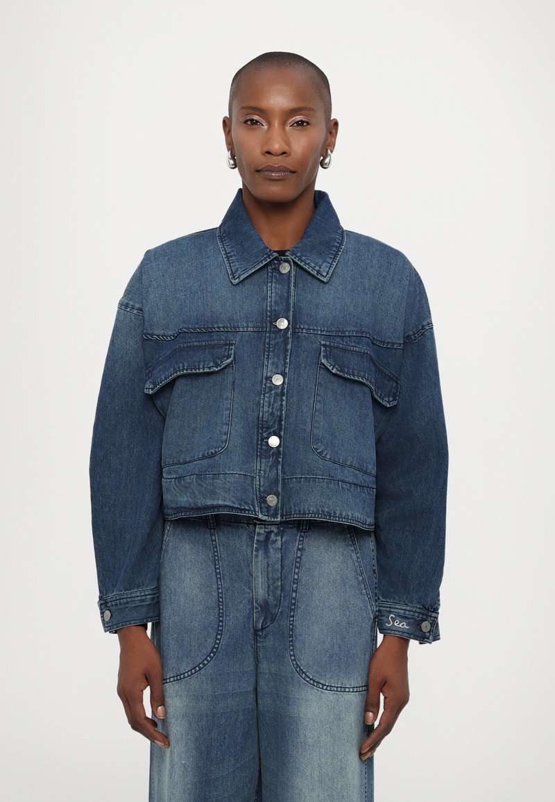 Kratka denim jakna v temno modri barvi z dvema žepoma na prsih, srebrnimi gumbi in kontrastnim platnom na rami in zgornjih rokavih.