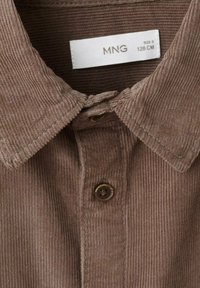Cămașă din corduroy maro, cu guler, două butoane și un model texturat al țesăturii. Eticheta de mărime indică MNG, mărimea 8, 128 CM.