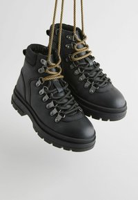 Czarne skórzane buty trekkingowe o teksturowanym wykończeniu, z metalowymi haczykami i złotymi sznurówkami oraz solidną, grubą podeszwą zapewniającą przyczepność.