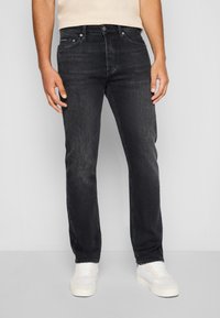 Jean en denim noir avec une coupe droite, caractérisé par un style à cinq poches et une texture légèrement décolorée, porté avec des baskets blanches.
