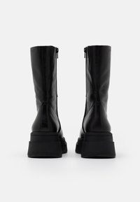 Bottes montantes en cuir noir au fini mat, dotées d'une semelle plateforme épaisse et d'une fermeture éclair verticale sur les côtés extérieurs.