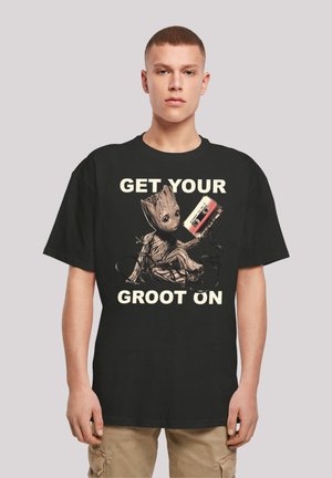 Black cotton t-shirt featuring a graphic of a cartoon character with exaggerated features and a cassette tape, accompanied by text in cream color.
