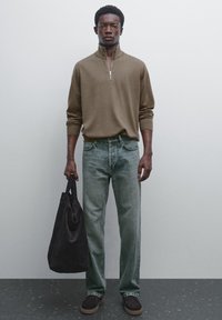 Brown zip-neck sweater, light green jeans, black tote bag, and dark shoes. The outfit features casual textures and relaxed fit.