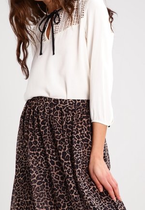 Weiße Bluse mit Spitzenpasse und schwarzer Krawatte, kombiniert mit einem hoch taillierten Leopardenmuster-Rock, Hand des Models ruht auf dem Rock.