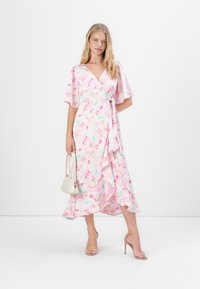 Φλοράλ φόρεμα τύπου wrap με φτερωτές μανίκες, σε παστέλ χρωματική παλέτα με ροζ, μπλε και λευκό, και με ρυθμισμένο στρίφωμα. Αξεσουάρ περιλαμβάνουν μια μικρή λευκή τσάντα.