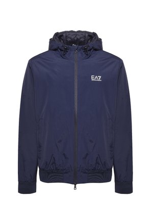 Námornícky modrá vetrovka má zips vpredu, elastické manžety a kapucňu so sťahovacou šnúrkou. Na hrudi je logo EA7, má hladkú textúru a je vyrobená z ľahkého materiálu.