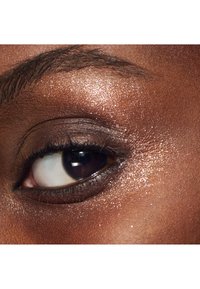 Close-up van een oog met een glanzend bruine ooglid, donkere wimpers en een glanzende, sprankelende huidstructuur rondom het oog.
