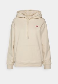 Sweat à capuche beige en tissu doux, avec une poche avant, une capuche à cordon de serrage, et un petit patch logo rouge sur la poitrine.