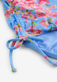 Tela azul con estampado floral rosa, detalle fruncido y cordón ajustable en una sección ampliada de una prenda de vestir.