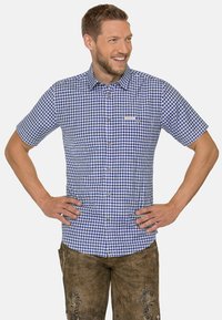 Kurzärmliges, blau-weiß kariertes Hemd mit Button-Down-Kragen und Brusttasche. Getragen mit braunen gemusterten Shorts.