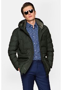 Zielona pikowana kurtka z kapturem, z dwoma przednimi kieszeniami i zapięciem na zamek. Noszona na niebieskiej koszuli w kwiaty z zapięciem na guziki.