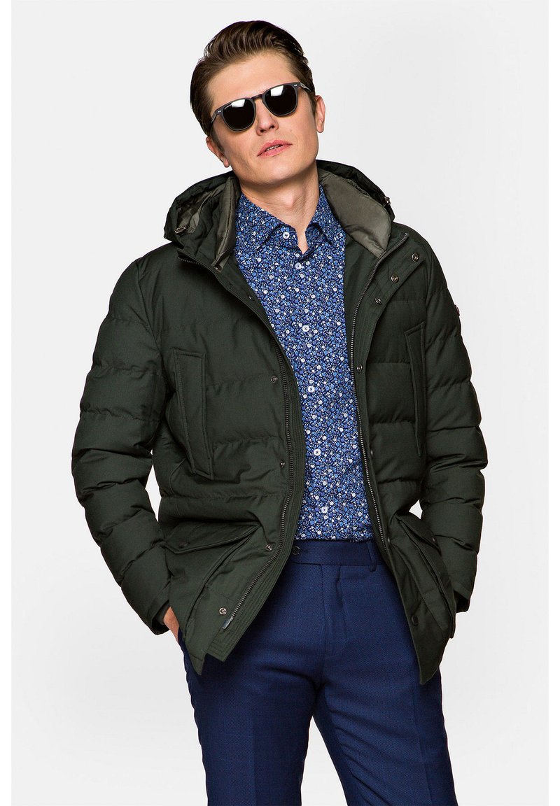 Zielona pikowana kurtka z kapturem, z dwoma przednimi kieszeniami i zapięciem na zamek. Noszona na niebieskiej koszuli w kwiaty z zapięciem na guziki.