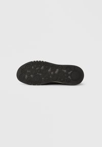 Semelle d'une chaussure noire présentant des motifs de traction circulaires de tailles variées sur un fond gris clair.