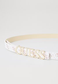 Ceinture blanche avec des accents à motifs roses, dotée d'une boucle en or portant le logo "GUESS". Fabriquée en matériau synthétique, avec une finition lisse et texturée.