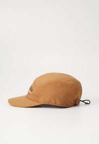 Barna nylon sapka ívelt visorral, a hátulján állítható zsinórral és elöl fekete logóval. Sima textúra.