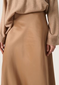 Brun kunstlæder nederdel med en glat tekstur, der falder fra en tætsiddende talje til en flared kant, båret med en lys beige strikket sweater.