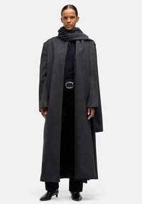 Długi, ciemnoszary płaszcz o szerokich rękawach, wykonany z grubego materiału. Noszony na czarny top i spodnie, z grubym, dopasowanym szalikiem. Czarne, spiczaste buty.