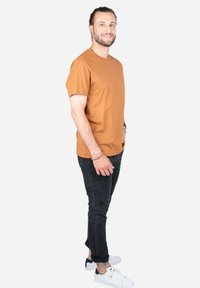 Bruine katoenen T-shirt met korte mouwen, gecombineerd met zwarte jeans en witte sneakers. Soepele textuur en relaxte pasvorm. Geen zichtbare logo's.