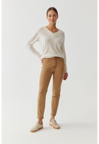 Suéter de cuello en v color beige claro combinado con pantalones ajustados color beige y zapatillas beige. La ropa está hecha de un tejido suave y tiene un diseño casual.