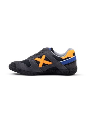 Zapatilla deportiva con parte superior de ante negro, acentos en un color naranja brillante en forma de 'X', y suela de goma texturizada. Presenta un forro gris y una franja azul.