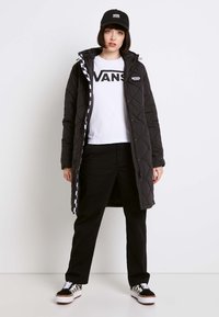 Černá prošívaná bunda s kapucí, bílý tričko s logem "VANS", černé kalhoty a černá čepice. Outfitu dodávají šmrnc tenisky s kostkovaným vzorem.
