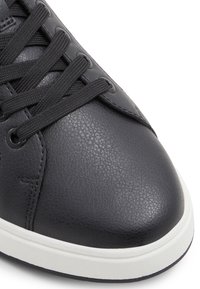 Sneaker nera in pelle con finitura texturizzata, suola in gomma bianca e lacci neri. Punta rotonda e dettagli di cucitura discreti sui lati.