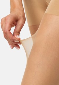 Bežové průhledné punčocháče tažené rukou, ukazující hladkou texturu a lehký materiál. Design má jemný povrch s mírným leskem.