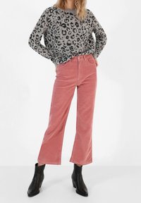 Grijze trui met luipaardprint, roze corduroy flared broek en zwarte enkellaarsjes. De trui heeft lange mouwen; de broek heeft een hoge taille.