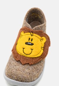 Filtshoe i brunt och grått med en gul lejonansikte-applikation på en brun accent. Slip-on-design med en texturerad yta och gummisula.