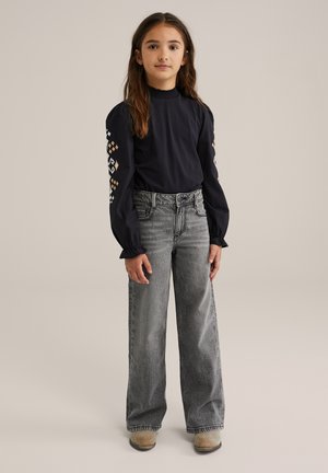 Maglia a maniche lunghe blu marino con dettagli decorativi sulle maniche, abbinata a pantaloni grigi a vita alta e a gamba larga. Le scarpe beige completano il look.