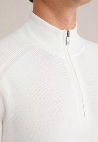 Weißer Reißverschluss-Pullover mit hohem Kragen, strukturiertem Rippstrickstoff und einem silbernen Reißverschlussdetail am Ausschnitt. Glattes und tailliertes Design.