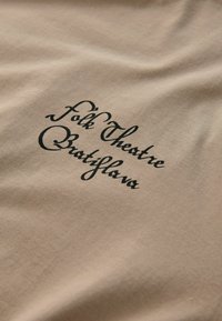 Bežikas kangas musta kalligraafia tekstiga, mis ütleb "Rahvateater Bratislava". Sile tekstuur, kergelt kortsus pind.