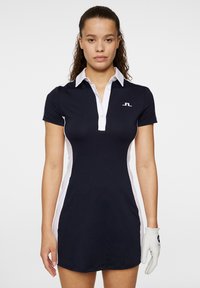 Marinblå pikétröja med vita accenter, korta ärmar och knappslå. Has en logotyp på bröstet och en figurnära silhuett. Strukturerad tyg.