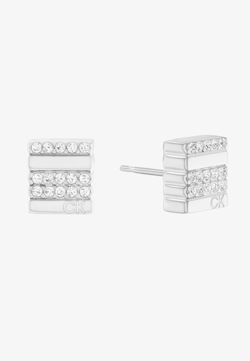 Boucles d'oreilles en argent avec une rangée horizontale de cristaux transparents, design empilé, et logo CK en relief sur le côté. Texture métallique lisse.