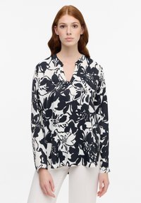 Top floreale in bianco e nero con scollatura a V, maniche lunghe e tessuto leggero. Presenta una vestibilità comoda e fessure laterali.