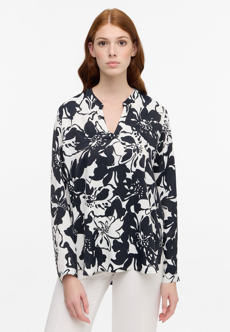 Top floreale in bianco e nero con scollatura a V, maniche lunghe e tessuto leggero. Presenta una vestibilità comoda e fessure laterali.