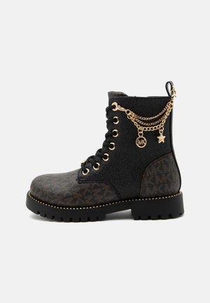 Botte de combat noire et marron avec laçage à l’avant, breloques chaîne dorée, semelle texturée et motif logo sur les panneaux des orteils et du talon.