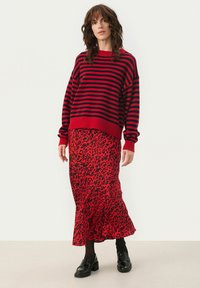 Pull surdimensionné rayé rouge et noir associé à une longue jupe léopard rouge. Porté avec des chaussures noires et des collants sombres.