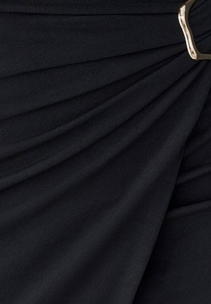 Tela negra con textura suave y diseño drapeado, que presenta pliegues y un detalle de hebilla dorada para el cierre.