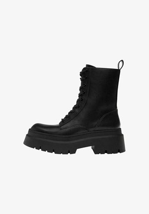 Černý vysoký vojenský kotník na šněrování s tlustou podrážkou a poutkem na zadní straně, zobrazený z boku na bílém pozadí.