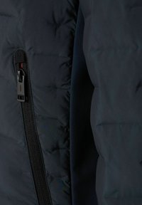 Schwarze Wattierte Jacke aus der Nähe, mit einer glatten Stoffoberfläche, horizontalen Nähten und einem kontrastierenden Reißverschluss mit roten Akzenten.