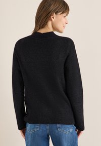 Maglione nero lavorato a maglia con finitura testurizzata, caratterizzato da un collo a giro e maniche lunghe, abbinato a jeans in denim blu.