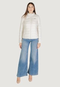 Lichtgewicht, gewatteerde witte jack met een hoge kraag, voor een ritssluiting en een klein logo-accent. Gecombineerd met wijde blauwe jeans.