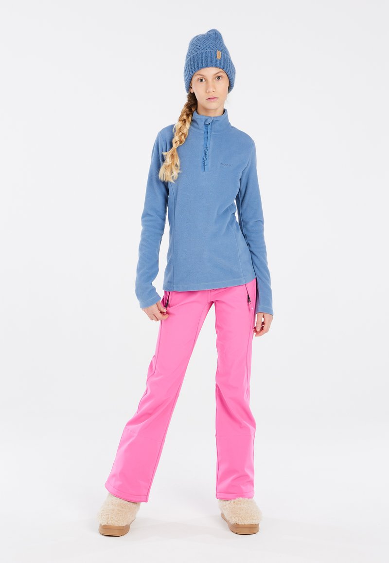 Pullover in pile blu con colletto alto e mezza zip, abbinato a pantaloni impermeabili rosa brillante e calzature in pelliccia beige.