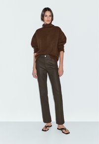 Brown oversized sweater with a high collar and ribbed cuffs, paired with dark brown straight-leg pants and black flat sandals.