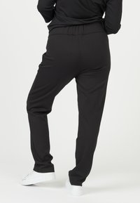 Zwarte joggers met elastische tailleband en een losse pasvorm, voorzien van een subtiele textuur en zijzakken, gecombineerd met witte sneakers.