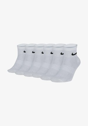 Calcetines de crew blancos hechos de una mezcla de algodón con textura acanalada, con un logo de Nike negro en cada calcetín. Seis pares exhibidos en fila.